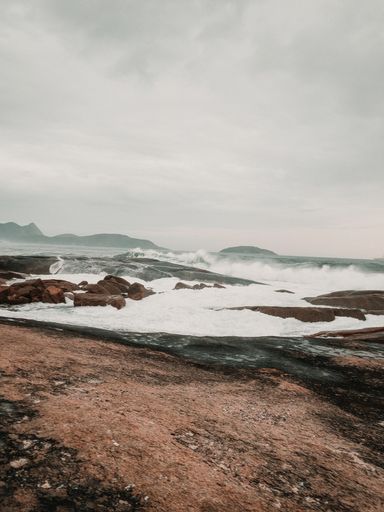 A vertical shot of the waves of the sea hitting the cliffs on the beach captured on a cloudy day