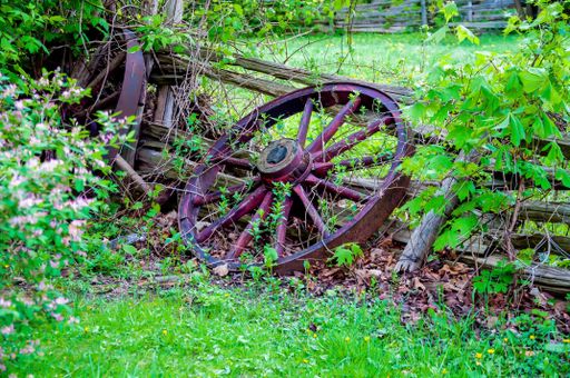 A broken wagon wheel leaned against a wooden fence on a grassy field