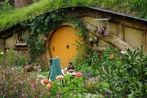 A beautiful shot of a small wooden house with an orange door surrounded by flowers and grass