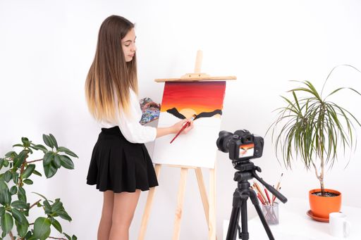 A beautiful young lady in an art studio painting on canvas with a brush in front of the camera