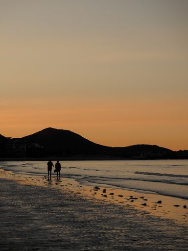 A vertical shot of a calm seashore with hills in the backgr