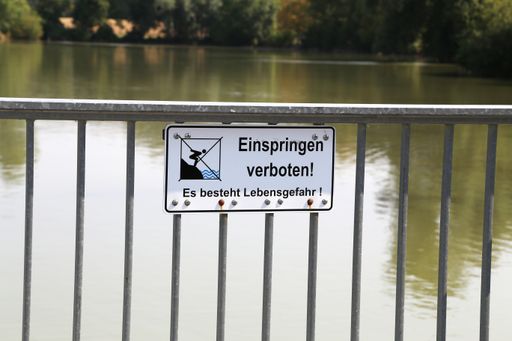A sign on the railing by the lake in German "Einspringen verboten! Es besteht Lebensgefahr", translation: "No jumping! Life-threatening danger"