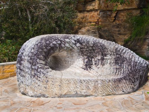 A modern grey concrete bench sits adjacent to a cliff face along a paved stone pathway