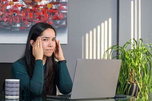 Tired South Asian woman having a business call at a desk, working on a laptop in home office