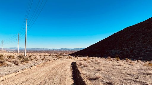 A scenic desert landscape featuring an empty road stretching into the distance and framed by electricity poles and distant mountain ranges