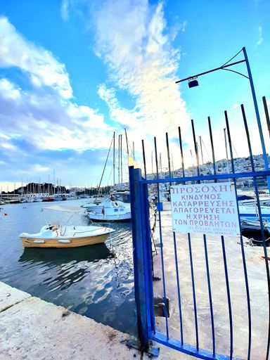 A blue metal gate with a 'CAUTION' sign with the port in the background, Athens, Greece