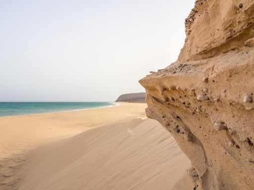 A beautiful shot of a rocky seacoast with soft sand and blue sea under the clear sky in Fuerte Ventura, Canary Islands