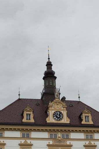 A vertical shot of a roof of the building with clock and statue - medieval central European architecture