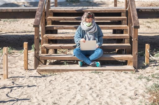 A closeup shot of a Spanish woman with her laptop sitting on wooden stairs on a sunny day