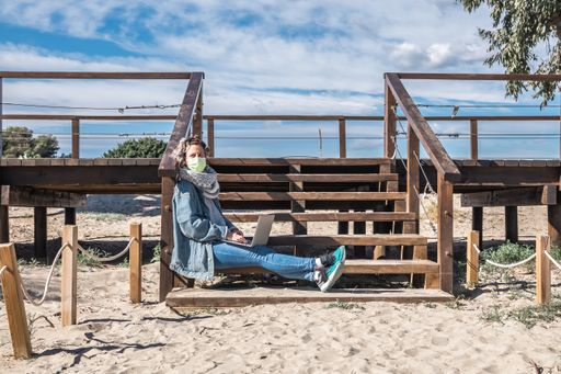 A closeup shot of a Spanish woman with her laptop sitting on wooden stairs on a sunny day
