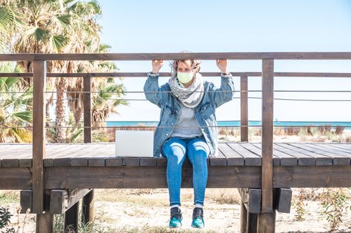 An Adult Caucasian woman with a facemask sitting on a wooden deck on the beach in Spain
