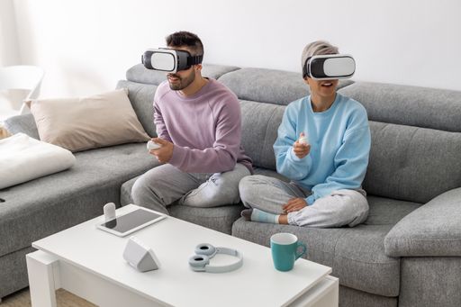 A young couple playing games with VR headsets while sitting on a sofa
