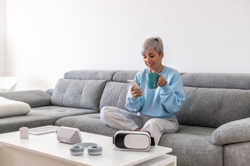 A young woman with short ppblonde hair sitting on a sofa and drinking coffee while using her phone