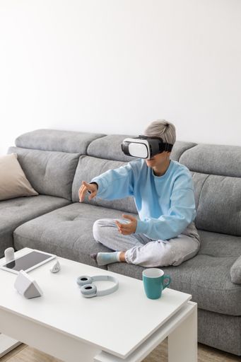An adult woman playing video games with a VR headset while sitting on the sofa