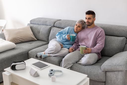 A young couple cuddling on a sofa and drinking coffee while watching TV