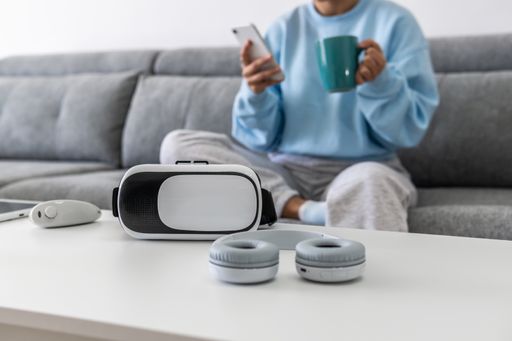 A female on the couch holding her phone and a mug, sitting in front of a table with gadgets