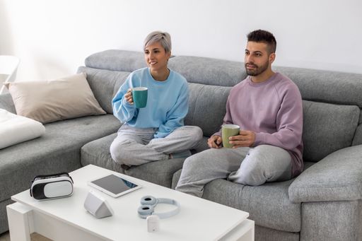 A young couple cuddling on a sofa and drinking coffee while watching TV