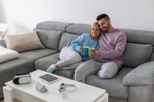 A cheerful young Spanish couple drinking coffee and enjoying the time together on the couch