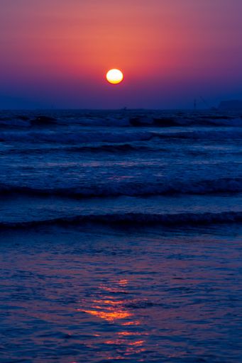 A vertical shot a wavy ocean under a dark sunset sky