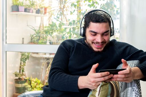 A shallow focus of a young Caucasian man playing a game on his smartphone while sitting on a couch in the living room at home