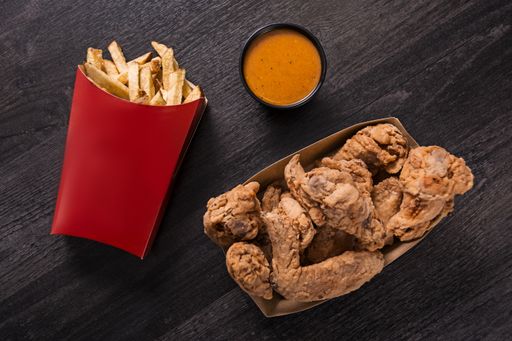 A top view of crispy fried chicken with french fries and sauce on a wooden table