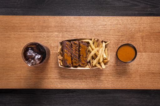 A top view of meat pieces with french fries, sauce and refreshing drink on wooden board