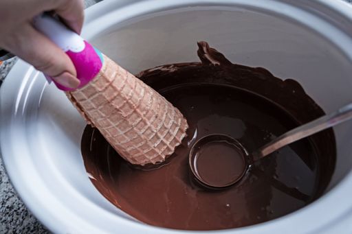 A female hand dipping waffle cone into melted chocolate