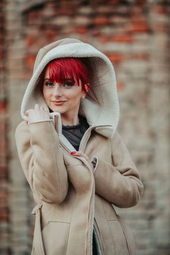 A portrait of a beautiful smiling red-haired woman with bangs wearing a warm winter coat with a hood over her head