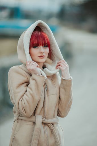 A portrait of a confident young red-haired girl with bangs looking at the camera wearing a warm winter coat holding the hood