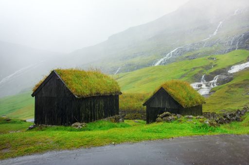 Foggy and rainy scenery from the landscape of the Faroe Islands - two wooden barns with grass-covered roofs.