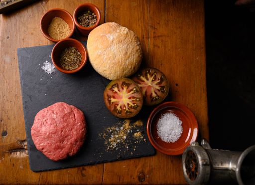 A high angle shot of the ingredients of a hamburger with a bun, tomato, minced meat and seasonings