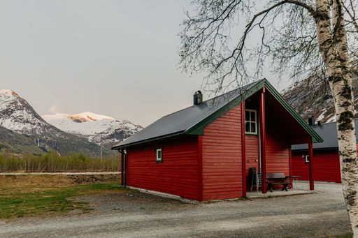 A wooden red cabin with a snow-covered mountain range in the background in Norway.