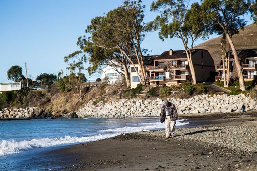 This is a stock photo of two people walking along the beach next to the water with houses in the background