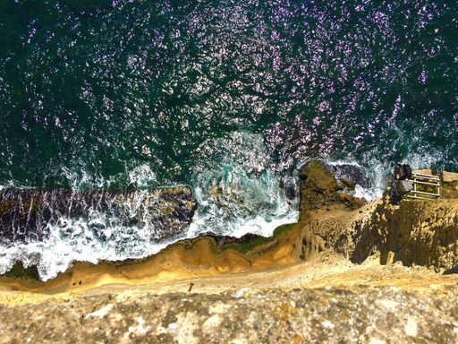 A high angle shot from the top of the cliff with sea waves hitting on the rock