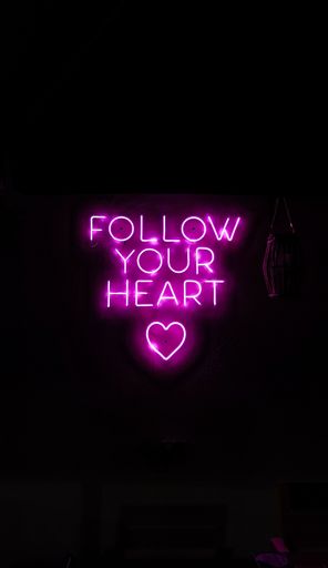 A vibrant purple neon sign featuring the phrase "Follow Your Heart" in a bold script font