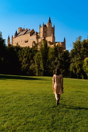 A young female walking in a lush green field with historic Alcazar Castle in the background