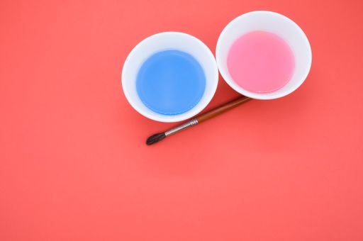 An overhead shot of paint wash bowls and a paintbrush on red background with space for your text
