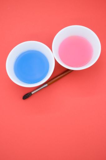 A vertical shot of paint wash bowls and a paintbrush on red background with space for your text