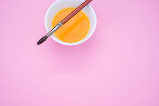 An overhead shot of a paint wash bowl and a paintbrush on pink background with space for your text