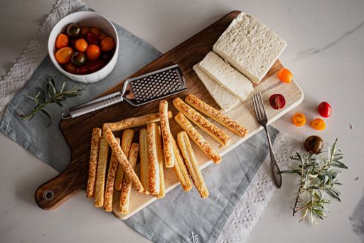 A top view of breadsticks with cheese and tomatoes on a wooden board