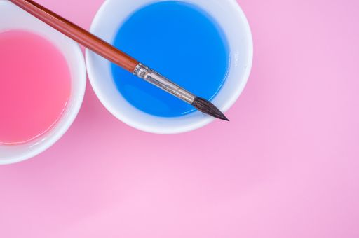 An overhead shot of paint wash bowls and a paintbrush on pink background with space for your text