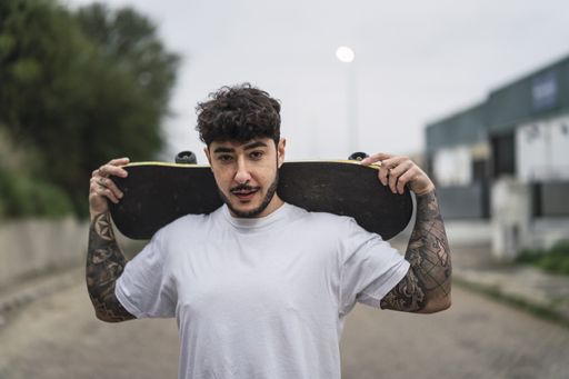 A young confident European male holding a skate on blurred background of a street