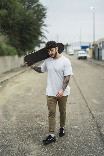 A vertical shot of a young confident European male holding a skate on blurred background of a street