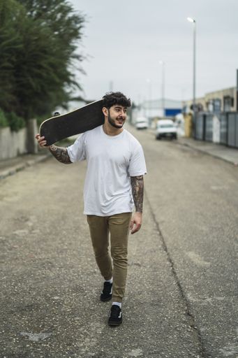 A shallow focus shot of a handsome smiling European skater posing with a skateboard in hands