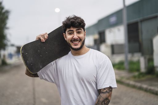 A young smiling European cool male holding a skate on blurred background of a street