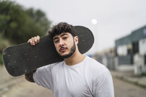 A shallow focus shot of a handsome European skater posing with a skateboard in hands