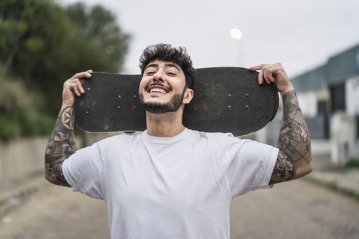 A young smiling European cool male holding a skate on blurred background of a street