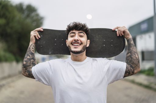 A shallow focus shot of a handsome smiling European skater posing with a skateboard in hands