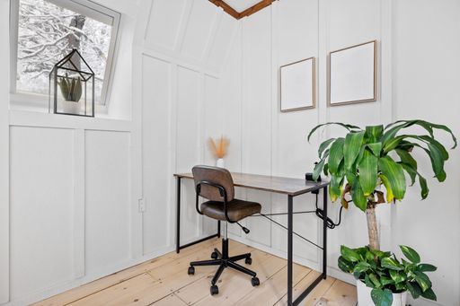 A wooden desk with a black metal chair and a plant on the corner