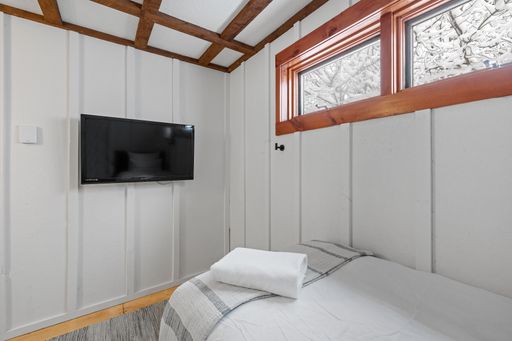 A comfortable white bedroom with a widescreen TV hanging on the wall